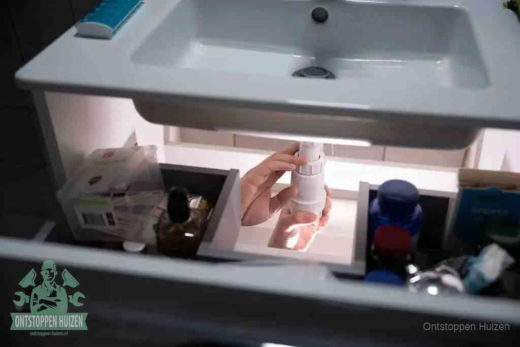 Een pompfles met zeep boven een wastafel, de heet water en afwasmiddel-methode om een vetprop in de afvoer los te maken in Huizen
