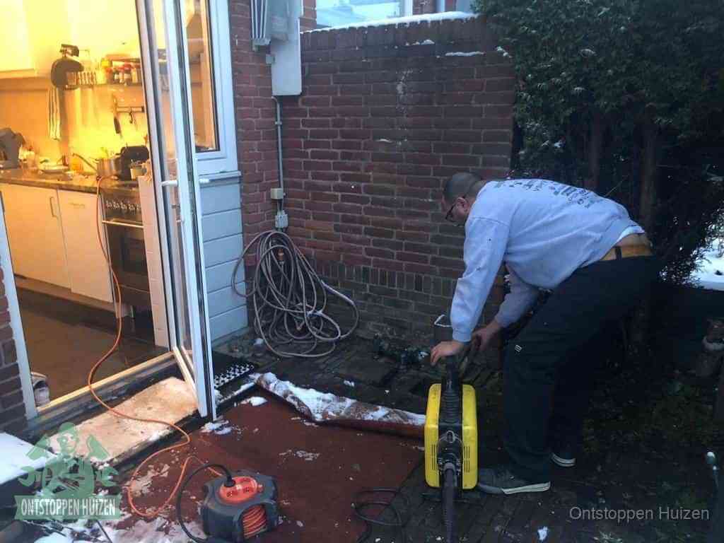 Een monteur werkt buiten bij een open riool-/grondput met een elektrische ontstoppingsmachine om een verborgen afvoerprobleem op te sporen in Huizen