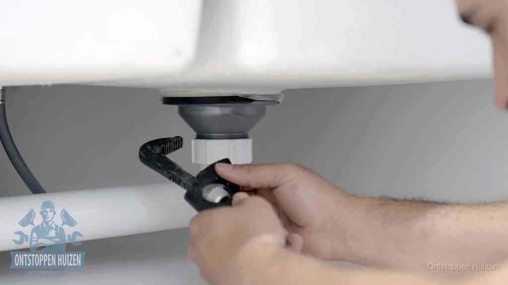 Twee handen draaien met een waterpomptang de wartelmoer van de kunststof sifon los om hem schoon te maken in Huizen