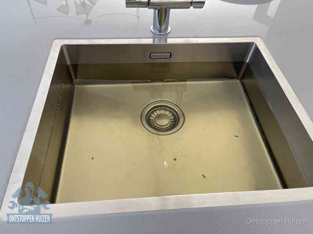 Stilstaand water in een rvs spoelbak dat niet wegloopt, een duidelijk signaal van een gootsteenverstopping in Huizen