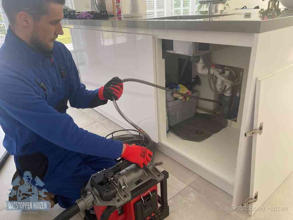 Een monteur reinigt de keukenafvoer grondig met een veermachine om terugkerende gootsteenverstoppingen te voorkomen in Huizen