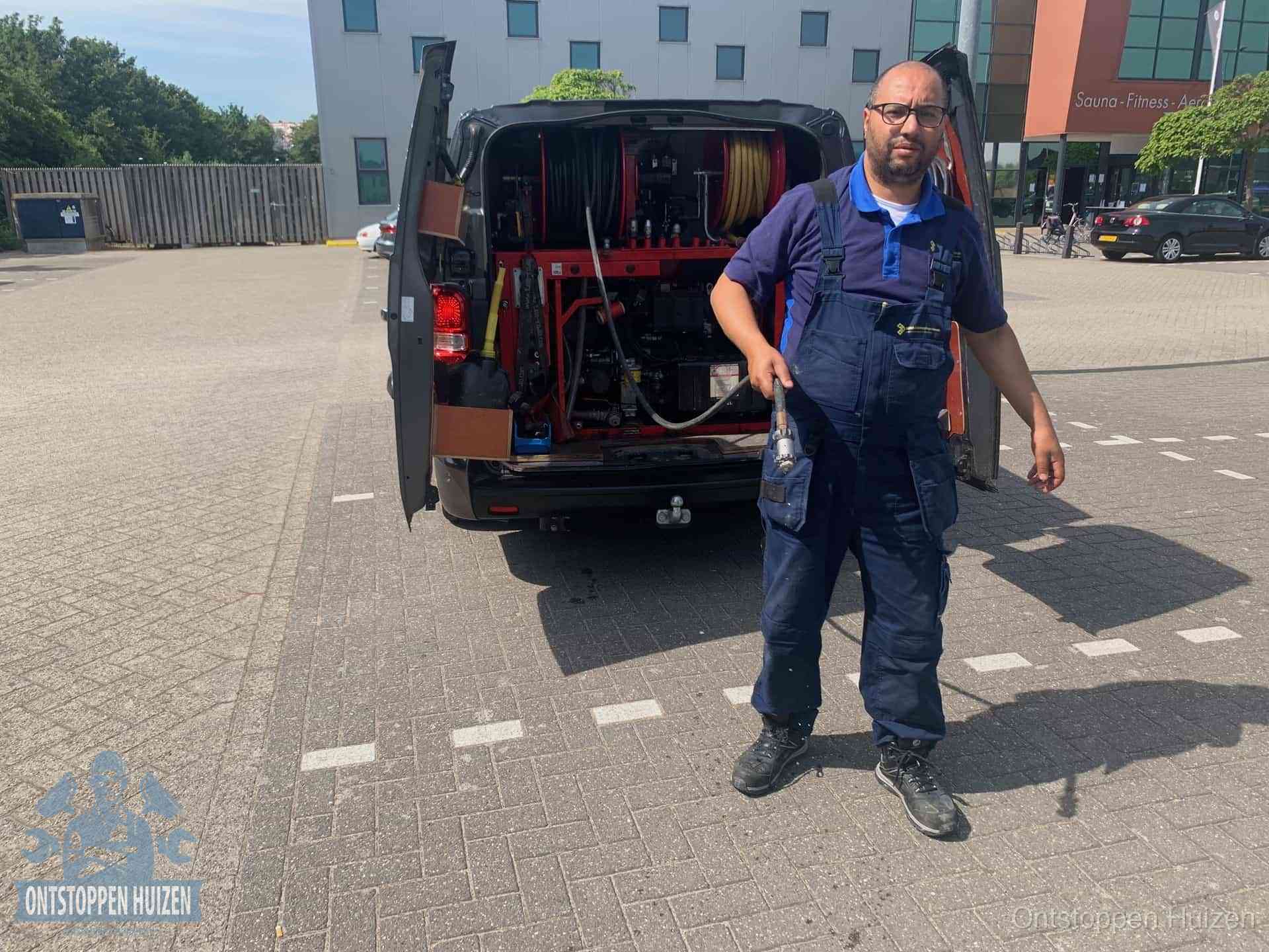 Een monteur bij zijn bestelbus met een hogedruk- en rioolreinigingsunit, klaar om de oorzaak van terugkerende wc-verstoppingen aan te pakken in Huizen