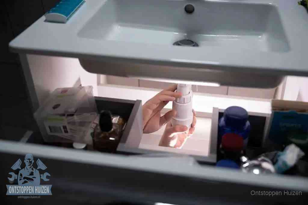 Een pompfles met zeep boven een wastafel in de toiletruimte, de warm water en afwasmiddel-methode om de wc te ontstoppen in Huizen