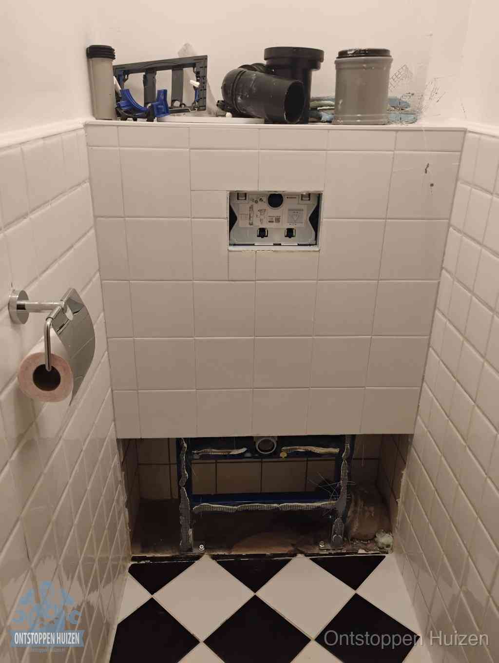 Een toiletruimte waar het hangtoilet en de inbouwreservoir-onderdelen zijn vrijgelegd voor onderhoud, periodiek nazicht voorkomt een wc-verstopping in Huizen