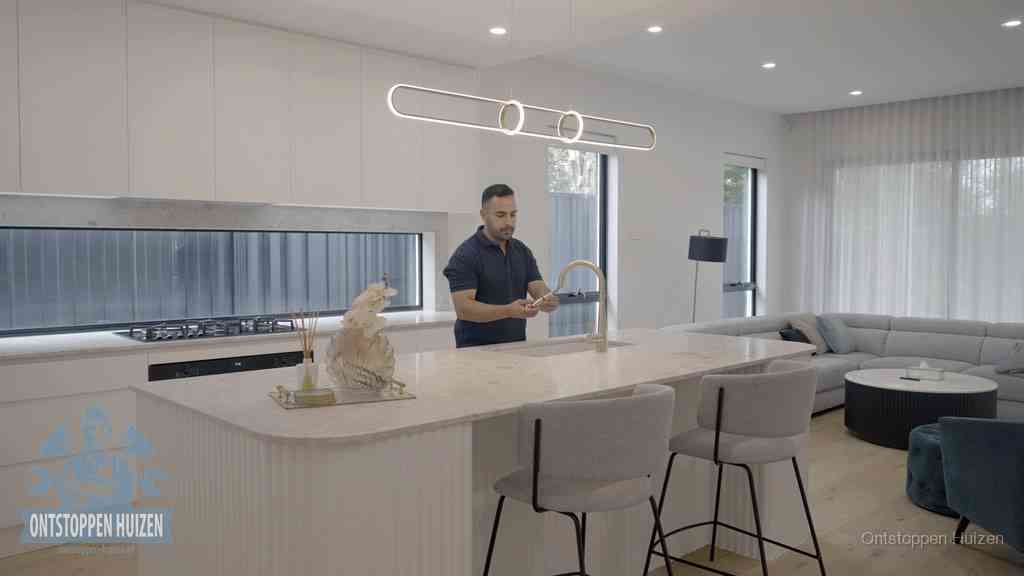 Een bewoner bij de keukenspoelbak die zelf aan de slag gaat met een verstopte gootsteen in Huizen