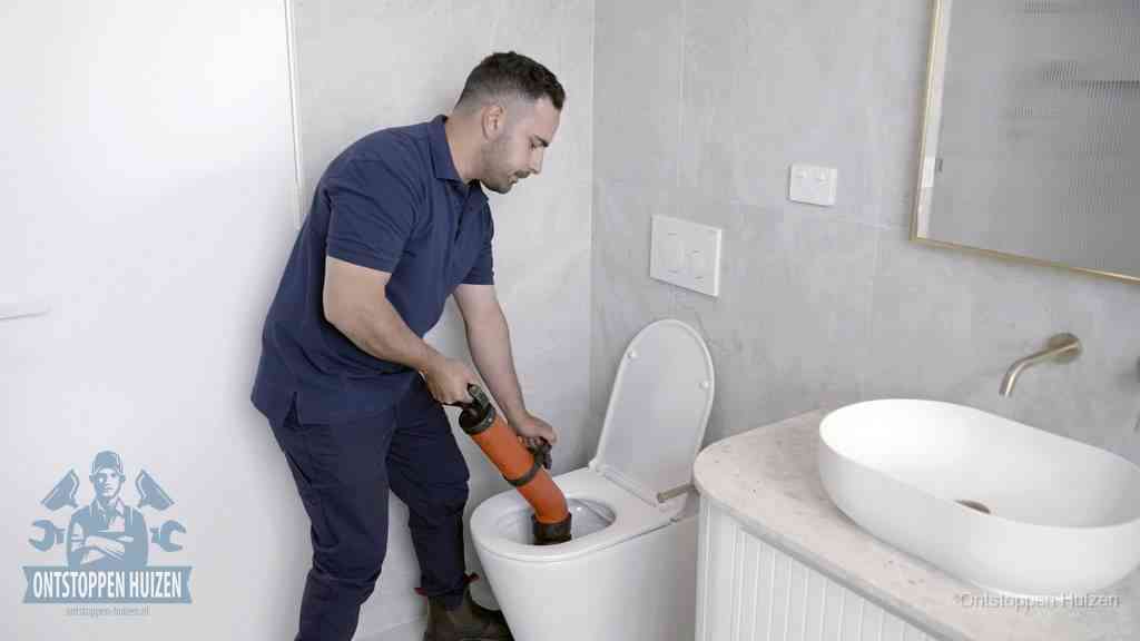 Een man gebruikt een handmatige luchtdruk-ontstopper in een modern betegeld toilet om zelf de wc te ontstoppen in Huizen